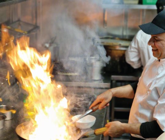 commercial kitchen with a chef cooking, the pan full of flames