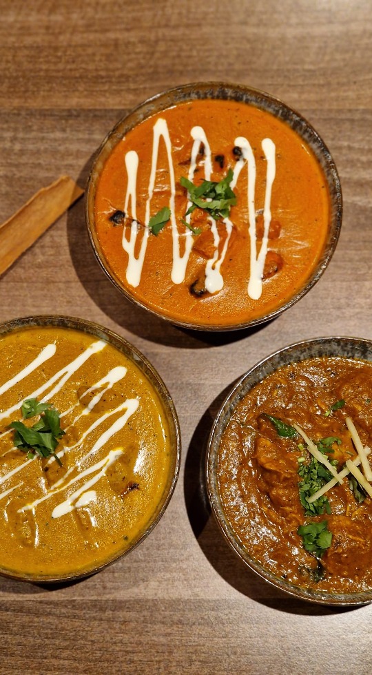 Three bowls filled with curry, garnished with cream and coriander